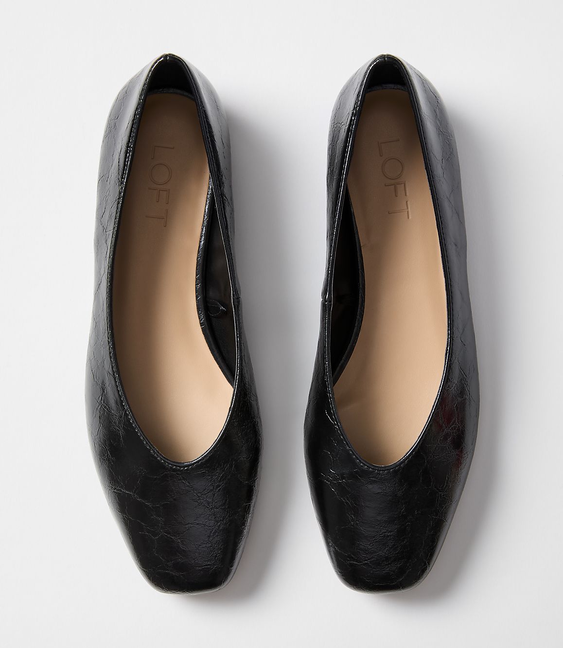 A pair of black leather ballet flats with a square toe sits on a plain white background.