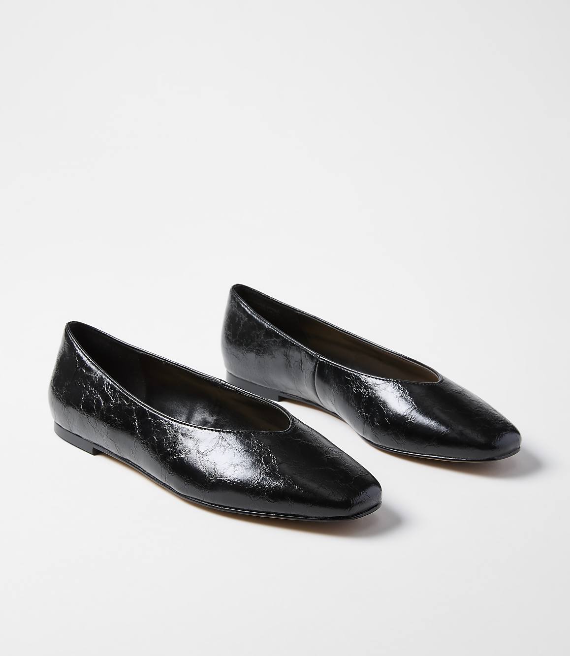 A pair of glossy black square-toe ballet flats rests on a plain white background.