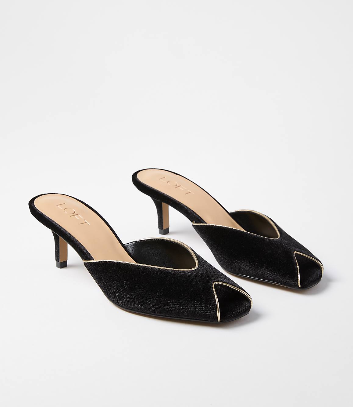 A pair of black velvet mules with gold trim are displayed on a plain white background.