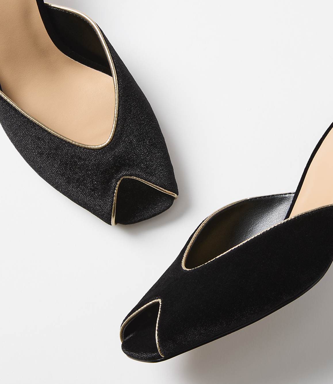 Two black velvet mules with gold trim are angled against a plain white background.