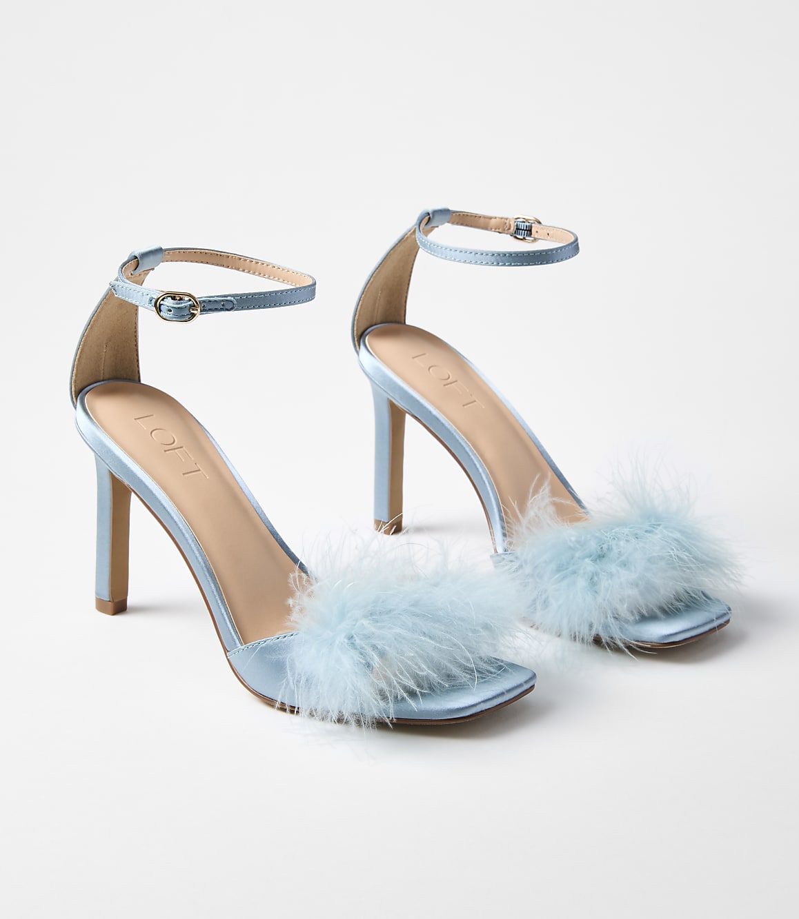 A pair of light blue satin heeled sandals with fluffy trim are displayed against a plain white background.