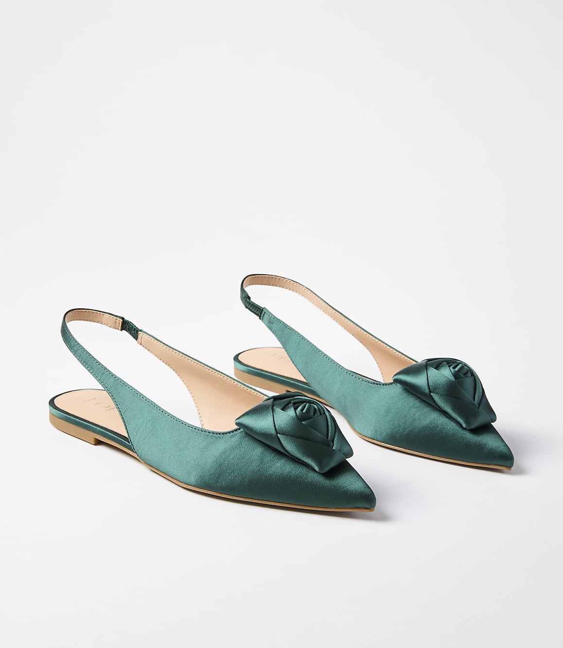 A pair of emerald green satin slingback flats with rose embellishments are displayed against a plain white background.