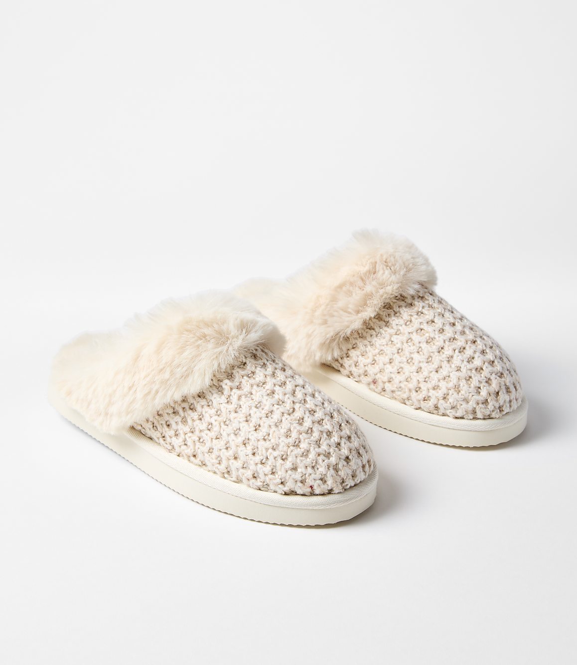 A pair of cream-colored, fuzzy slippers rests on a plain white background.