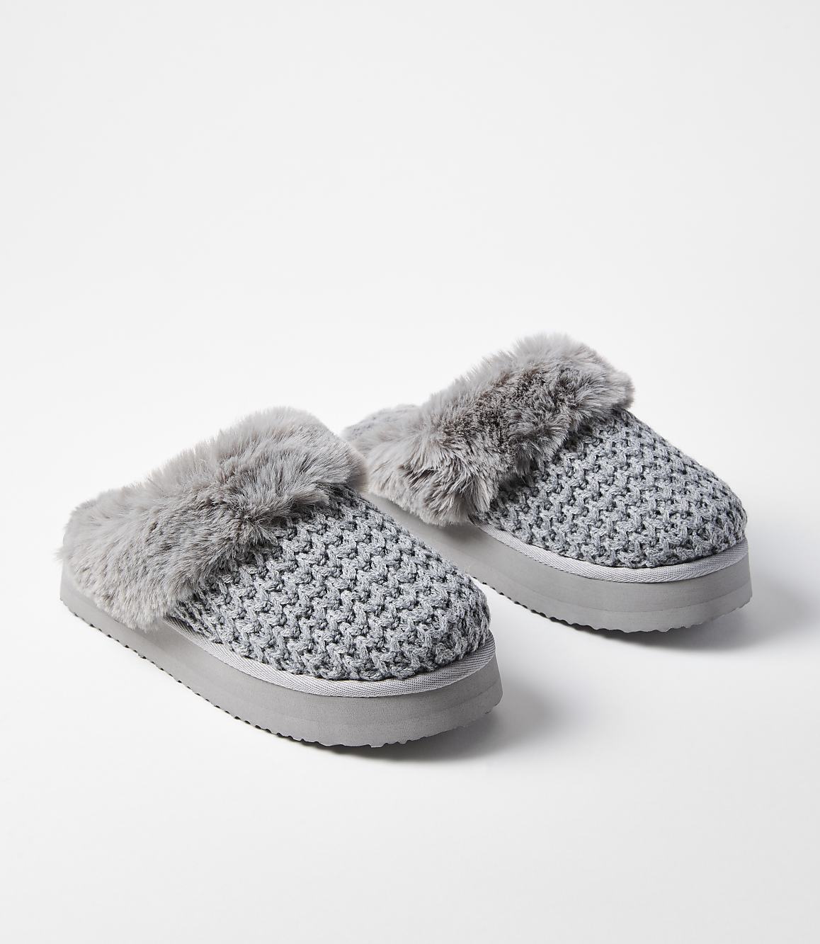 A pair of gray knitted slippers with faux fur trim rests on a white background.