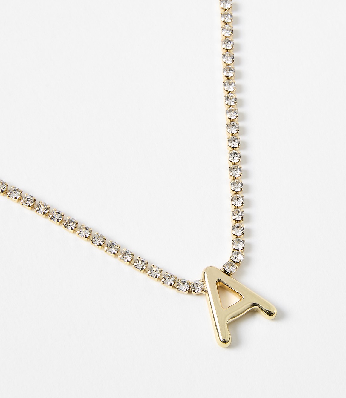 A gold necklace with a sparkling rhinestone chain and a prominent "A" pendant rests against a plain white background.