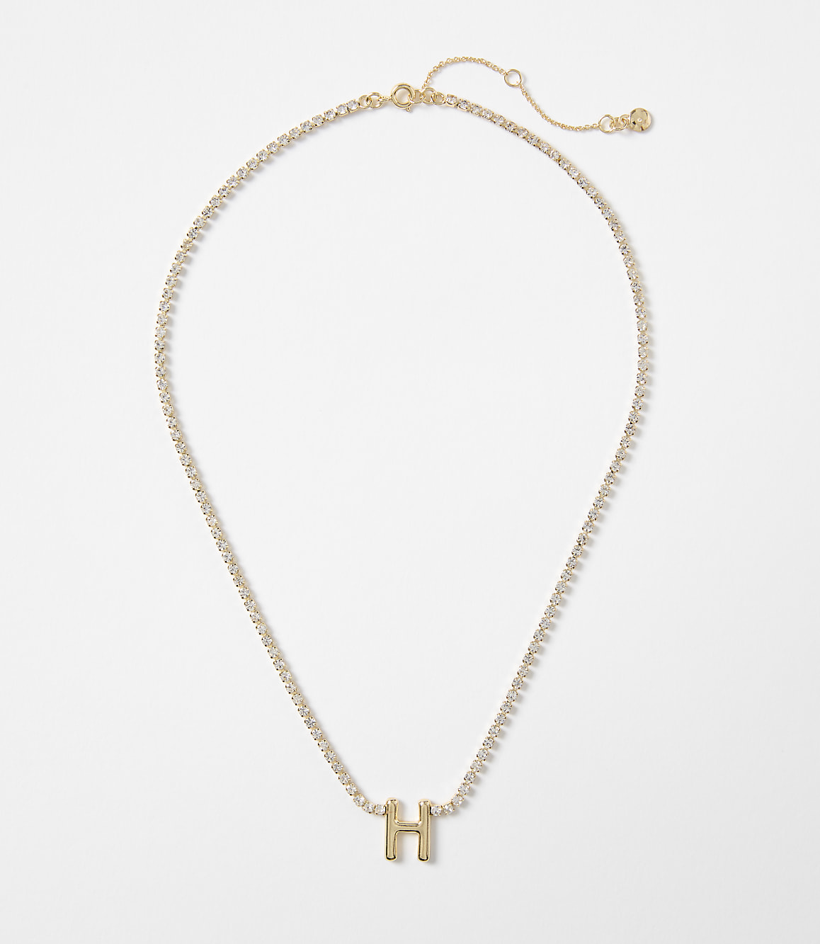 A gold necklace with a sparkling chain and a gold letter "H" pendant rests against a plain white background.