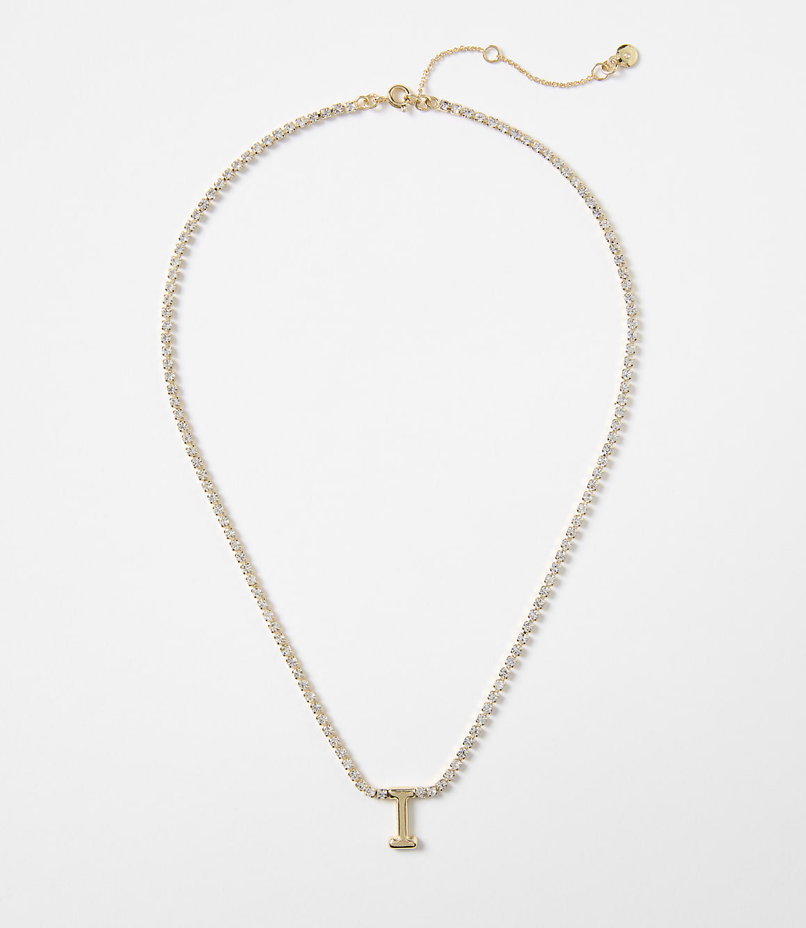 A delicate gold chain necklace with a sparkling "I" pendant rests on a plain white background.