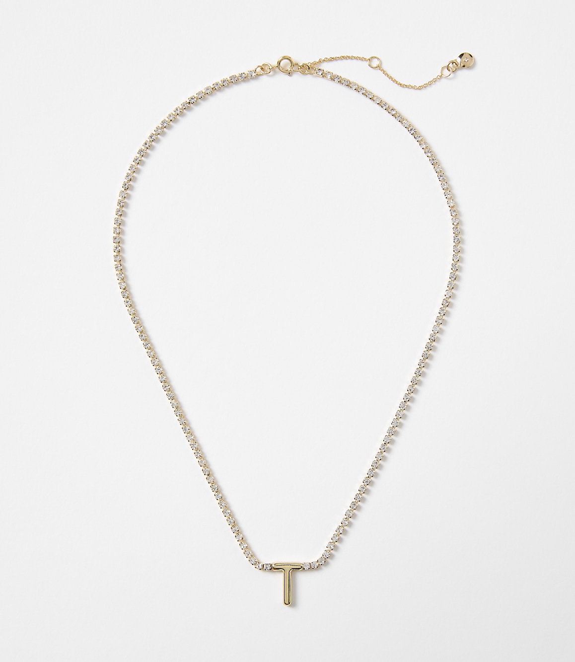 A delicate gold chain with a sparkling "T" pendant rests against a plain white background.