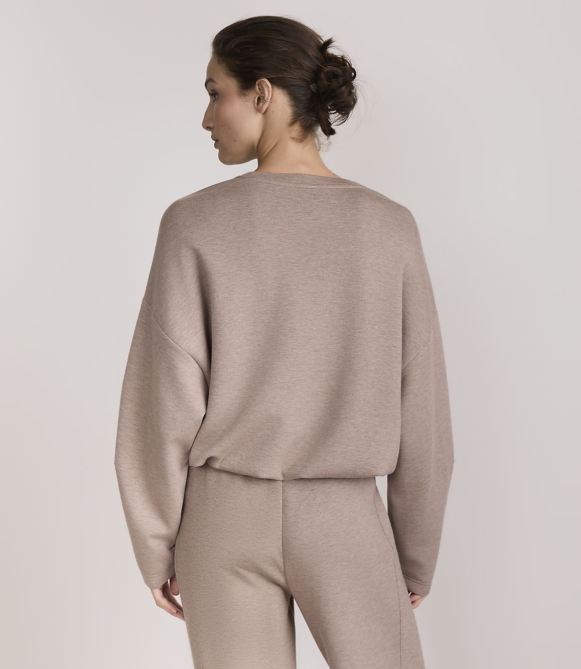 A woman in a taupe loungewear set stands against a plain, light gray background.