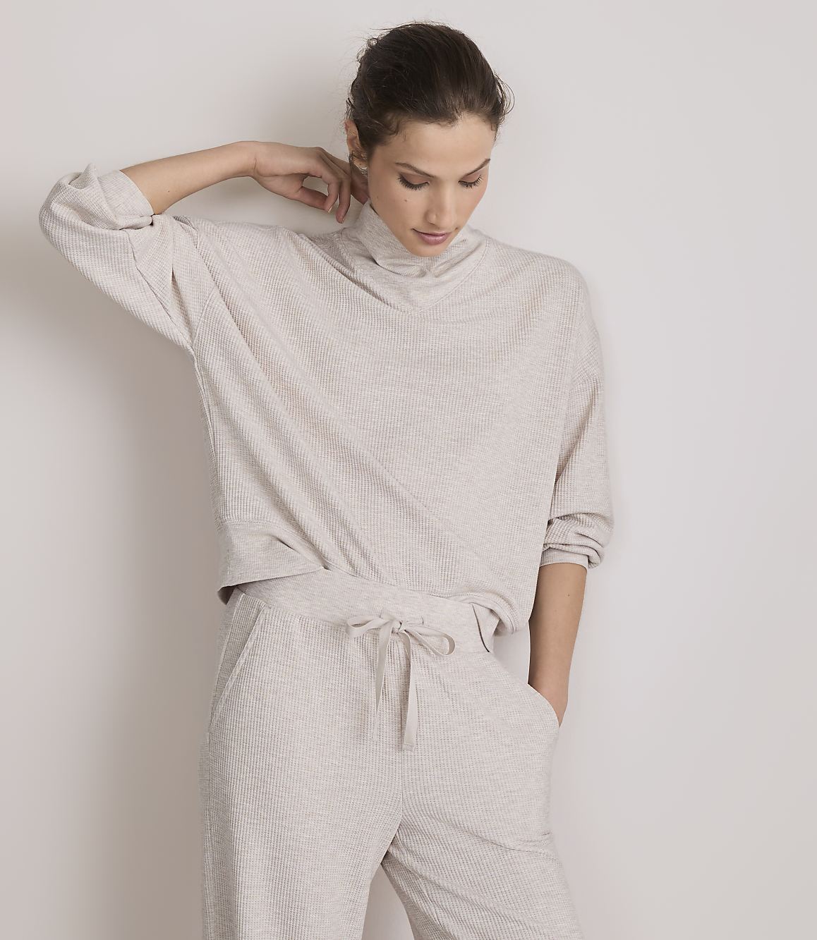 A woman in a beige loungewear set stands against a plain white background.