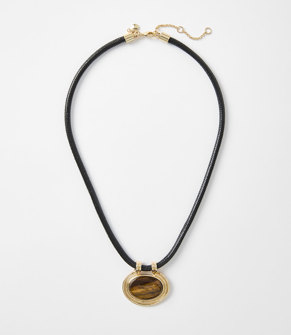 A black cord necklace with a gold-rimmed oval tiger's eye pendant hangs against a plain white background.
