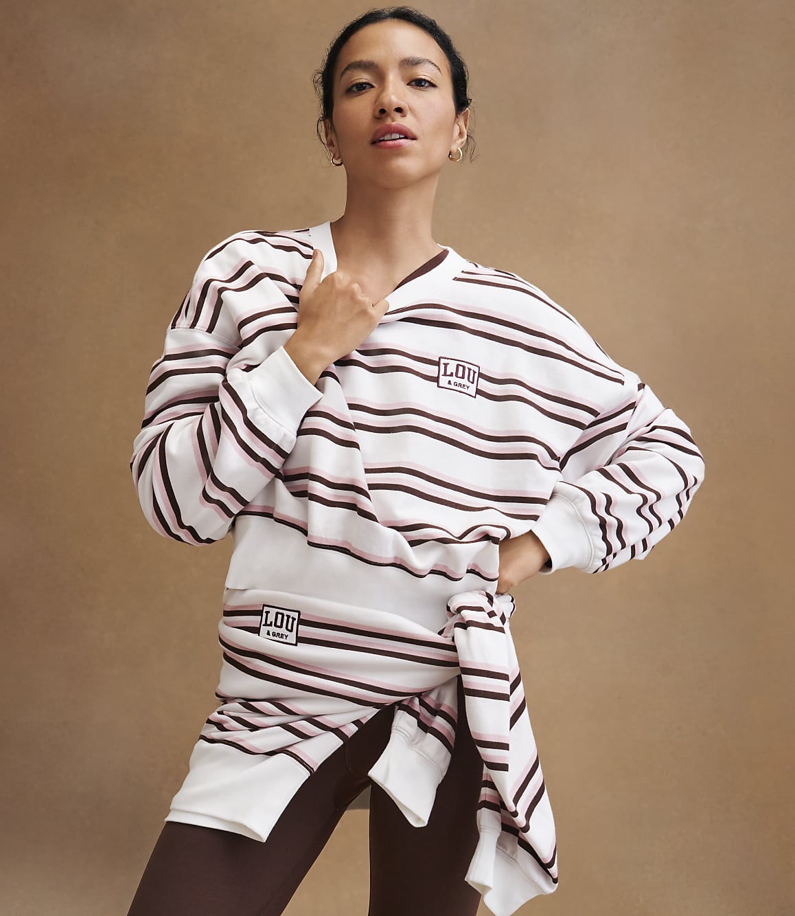 A woman in a striped sweatshirt and leggings stands against a plain brown background.