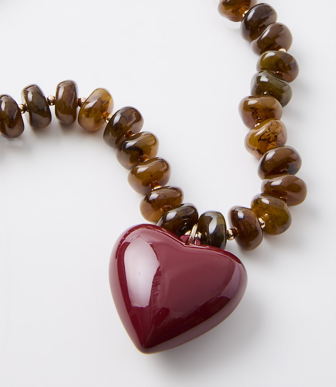 A glossy red heart pendant hangs from a strand of translucent brown beads against a plain white background.