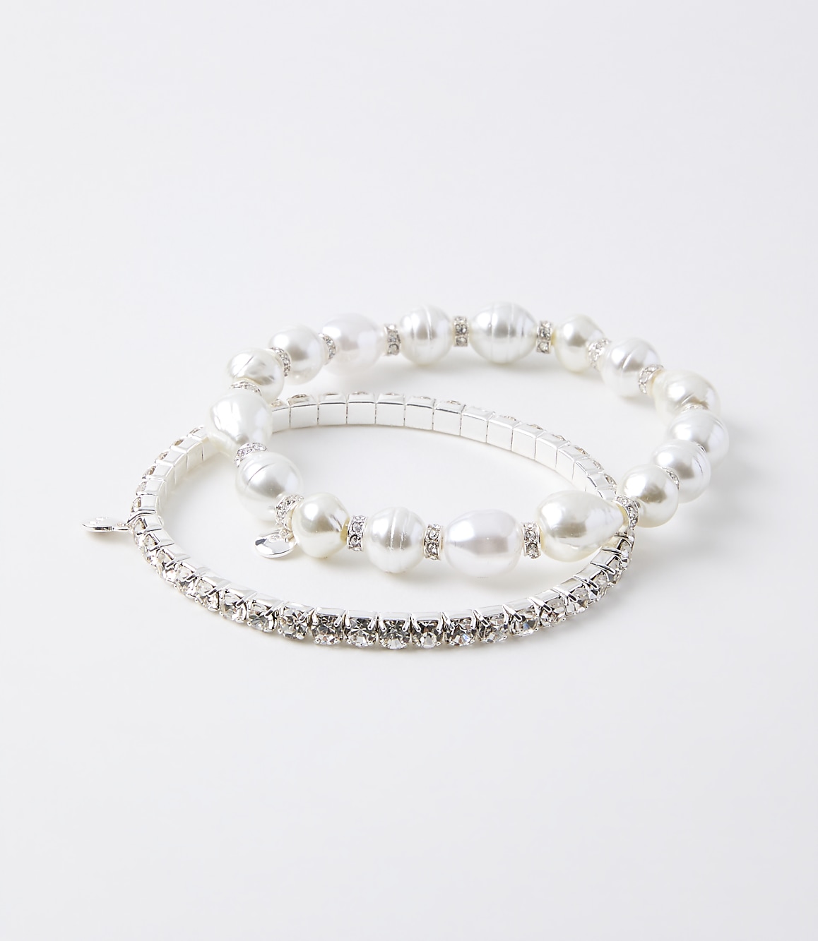 Two bracelets, one with pearls and rhinestones and another with only rhinestones, rest on a plain white background.