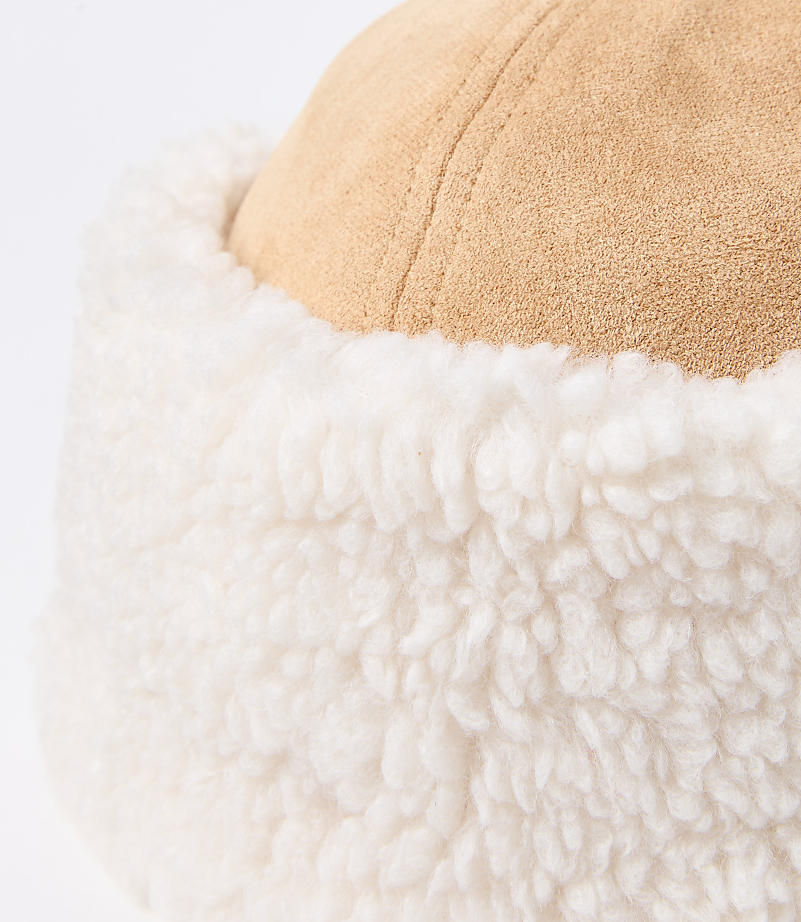 A close-up of a tan suede hat with a fluffy white trim is set against a plain white background.