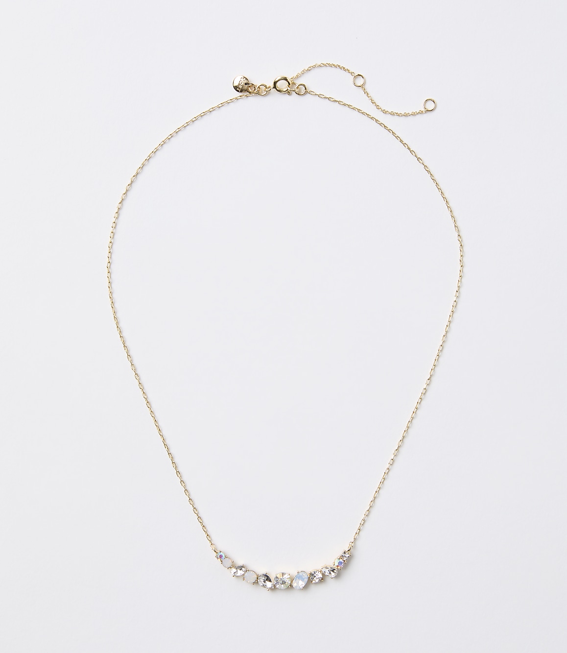 A delicate gold necklace with a curved arrangement of small, iridescent stones rests on a plain white background.