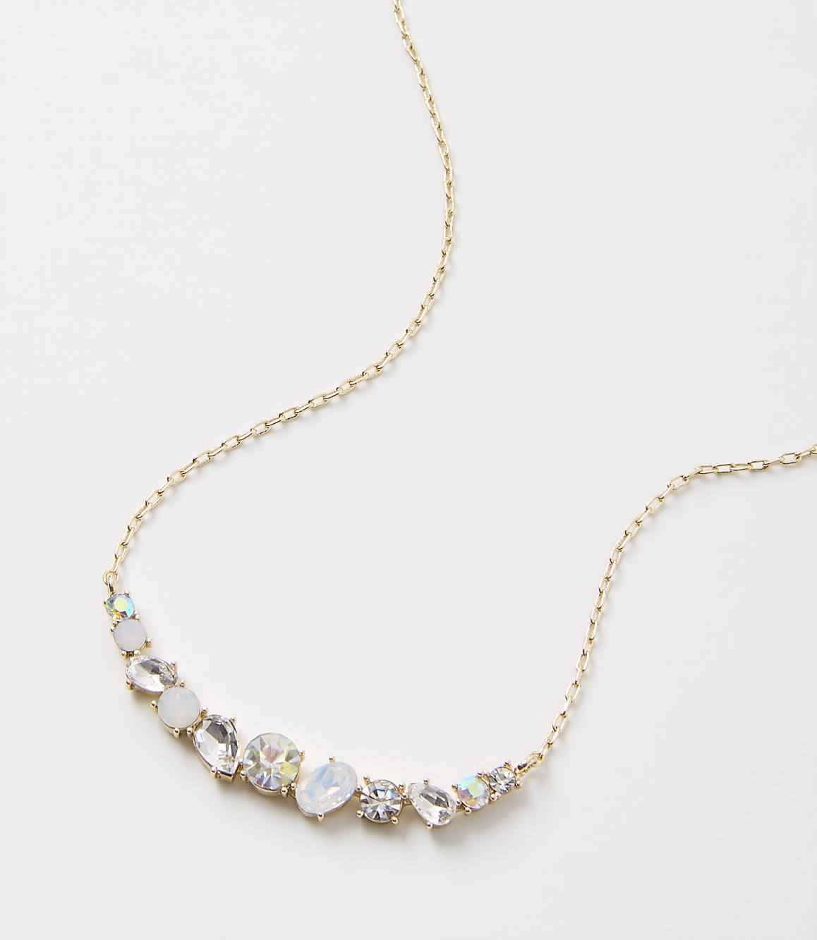 A delicate gold chain necklace with an assortment of clear and iridescent gemstones is displayed against a plain white background.