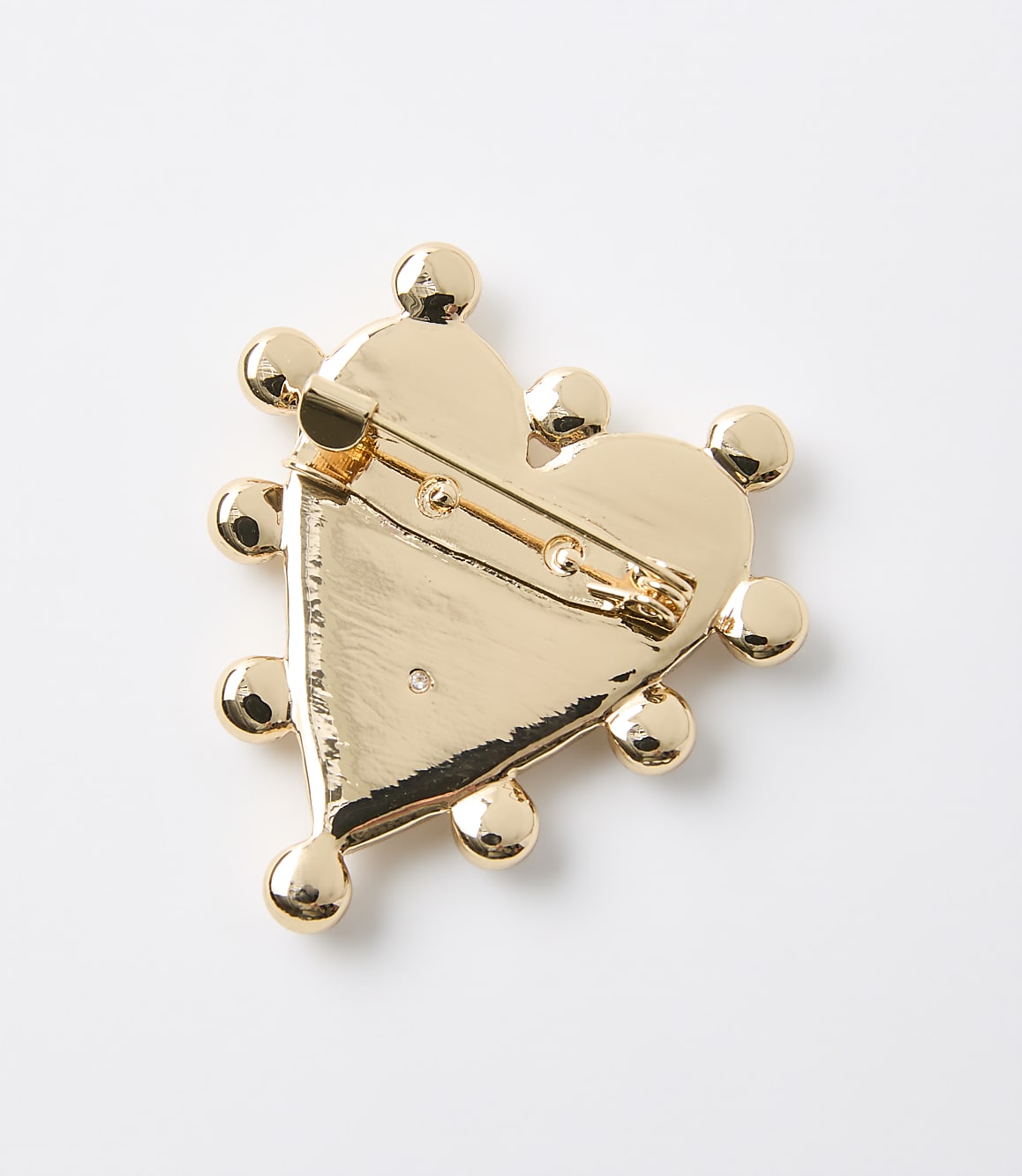 A gold heart-shaped brooch with decorative spheres around its edge is displayed against a plain white background.