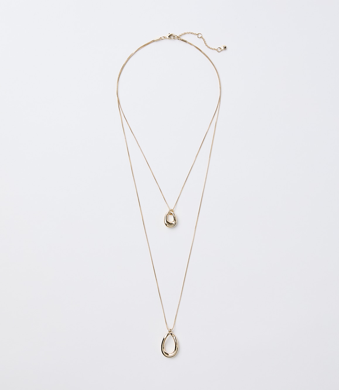A delicate gold layered necklace with two abstract pendant shapes hangs against a plain white background.