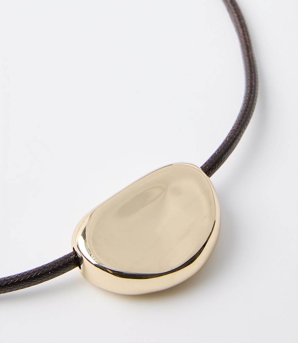 A smooth, golden pendant rests on a dark brown cord against a plain white background.