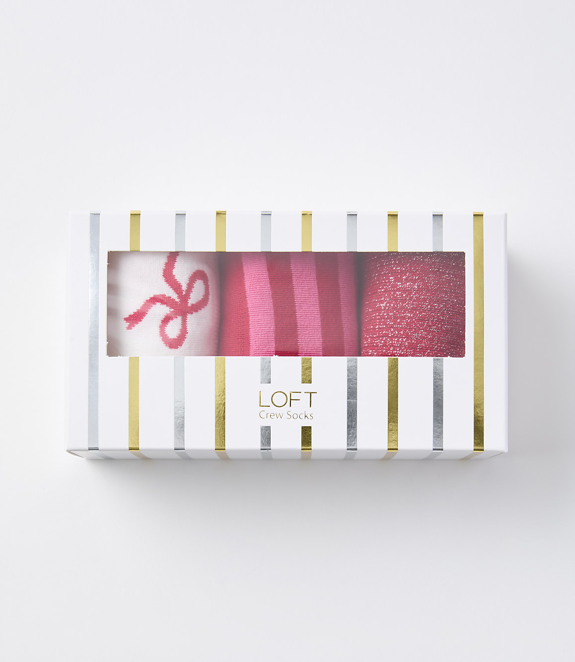 A white box with gold and silver stripes contains three pairs of pink socks, one with a bow, one striped, and one glittery, against a plain white background.