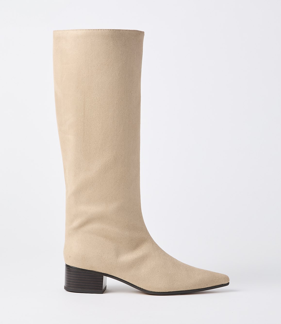 A beige suede knee-high boot with a pointed toe and a dark block heel stands against a plain white background.