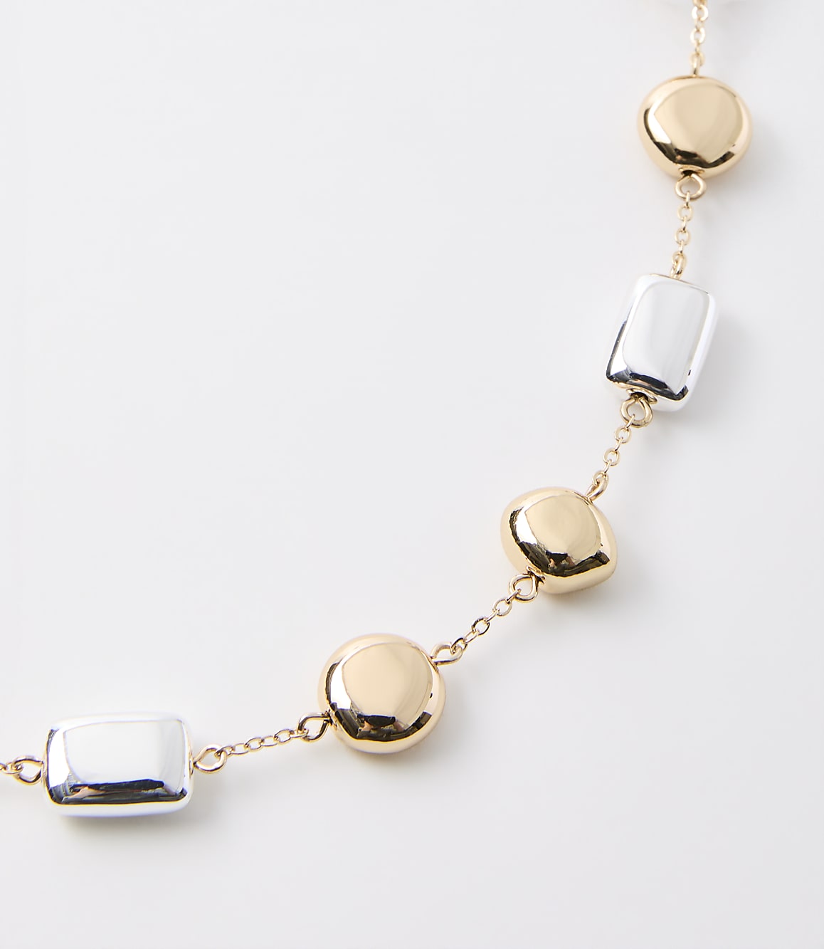 A delicate gold chain necklace with alternating polished gold discs and silver rectangular beads rests on a plain white background.