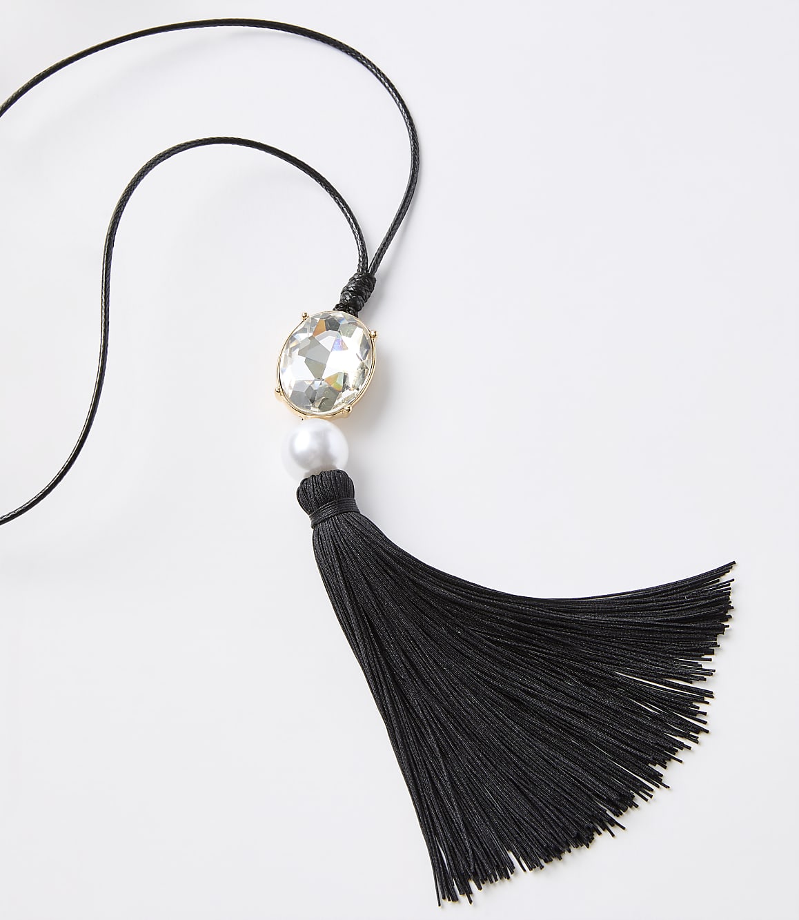 A black tassel necklace with a clear gem and pearl hangs against a plain white background.