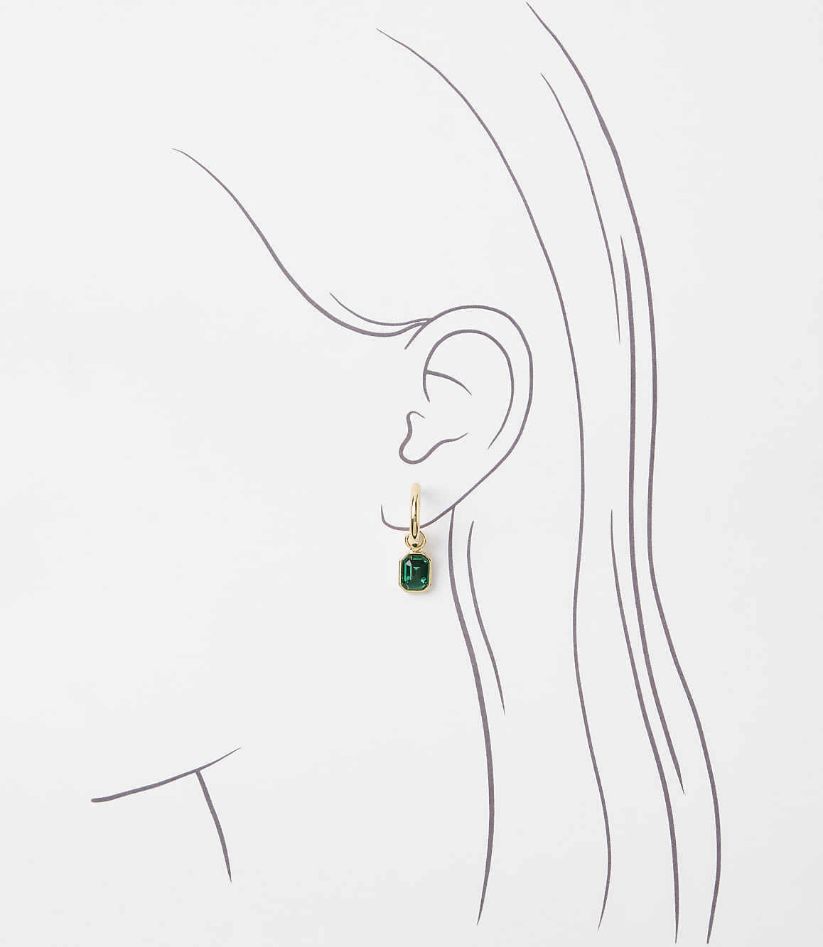 A delicate gold hoop earring with a small emerald gemstone dangles from a stylized outline of an ear against a plain white background.