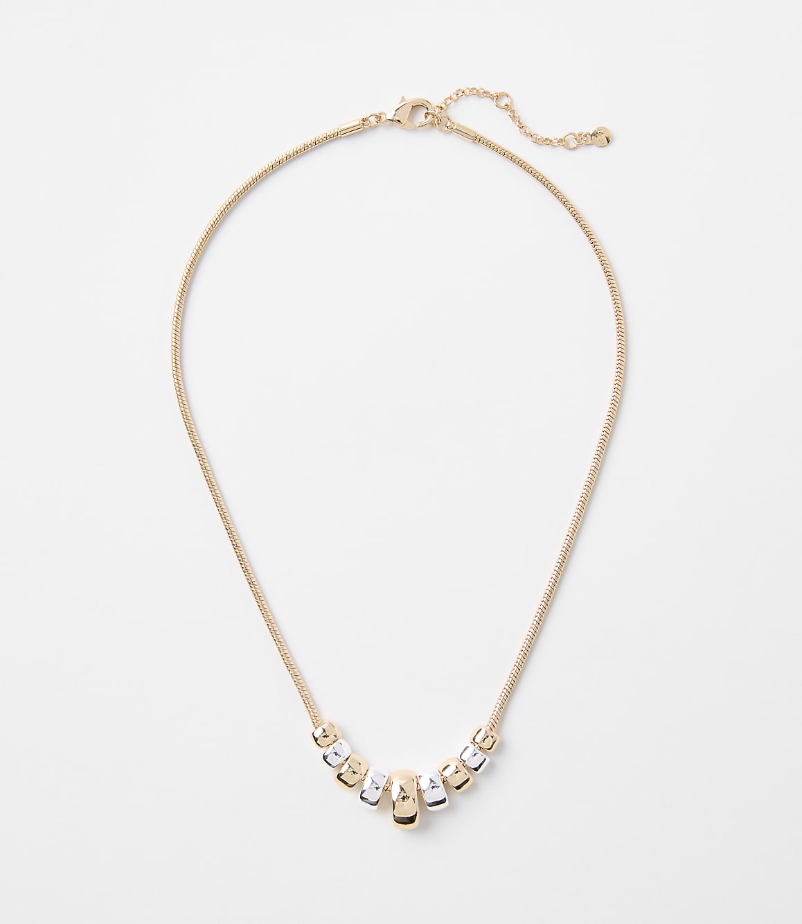 A delicate gold chain necklace with a series of alternating gold and silver cylindrical beads rests on a plain white background.