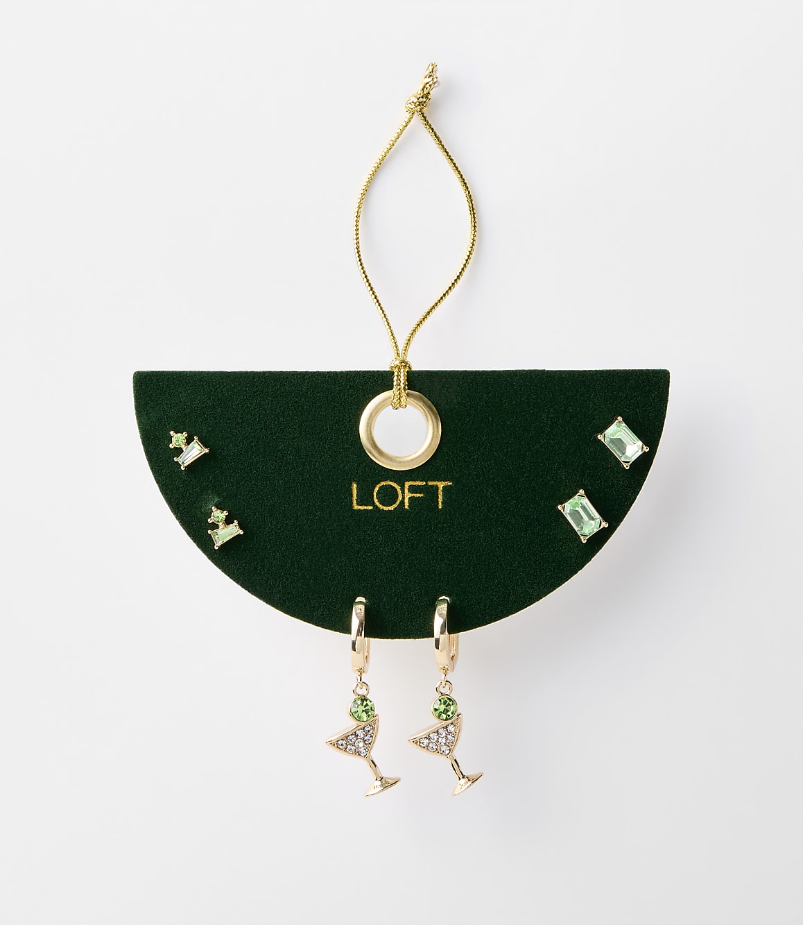 A set of green jeweled earrings, including martini glass and stud styles, are displayed on a dark green card with a gold loop and string against a plain white background.