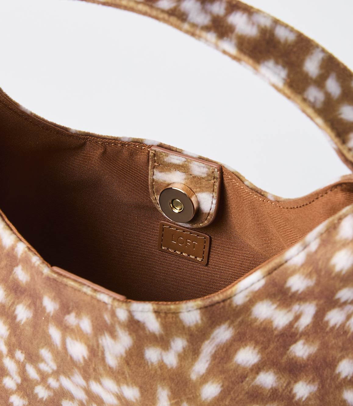 A close-up of a fawn-spotted handbag with a magnetic closure and brand tag is set against a plain white background.