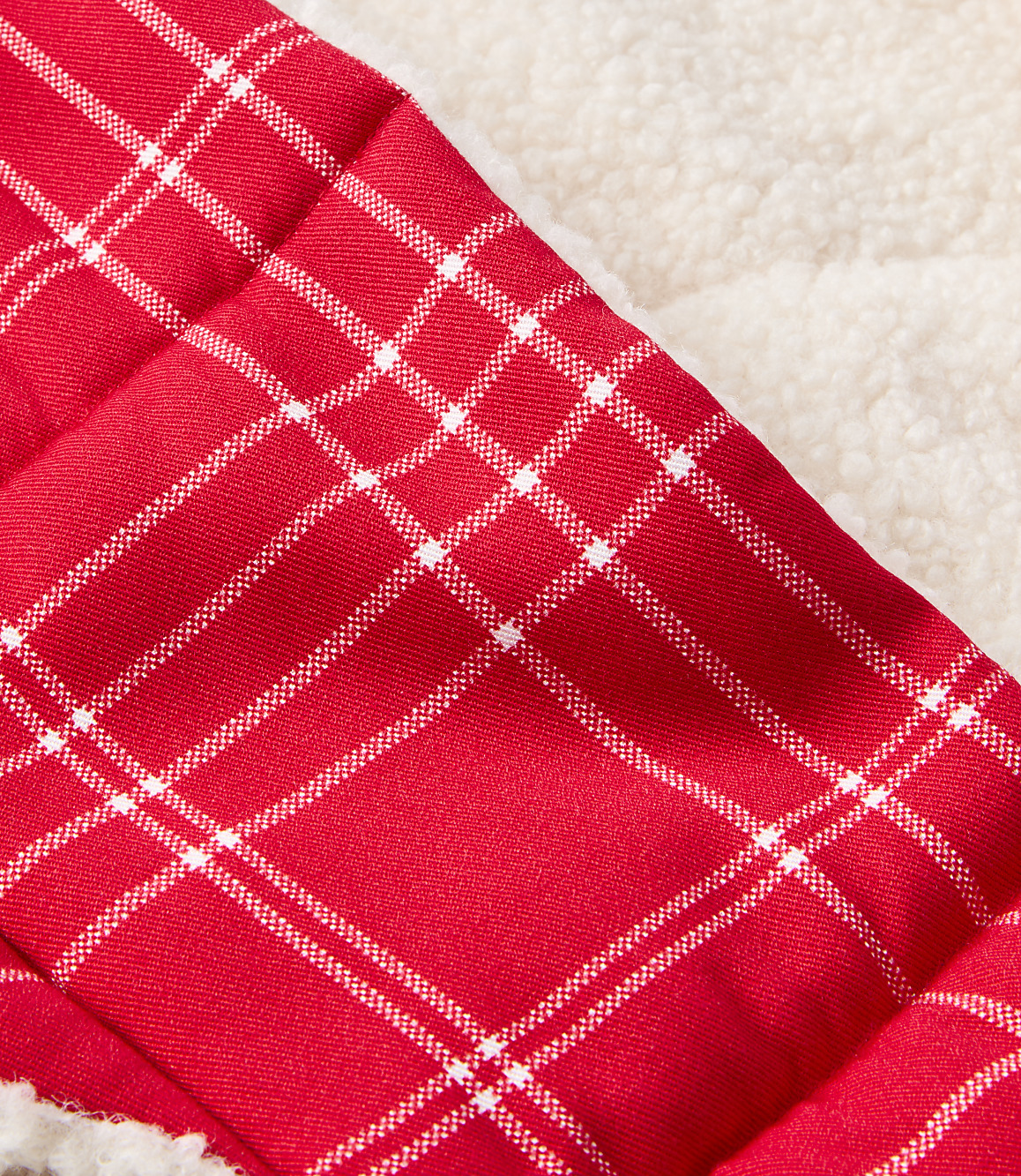 A close-up of red and white plaid fabric in the foreground is set against a soft, textured cream background.
