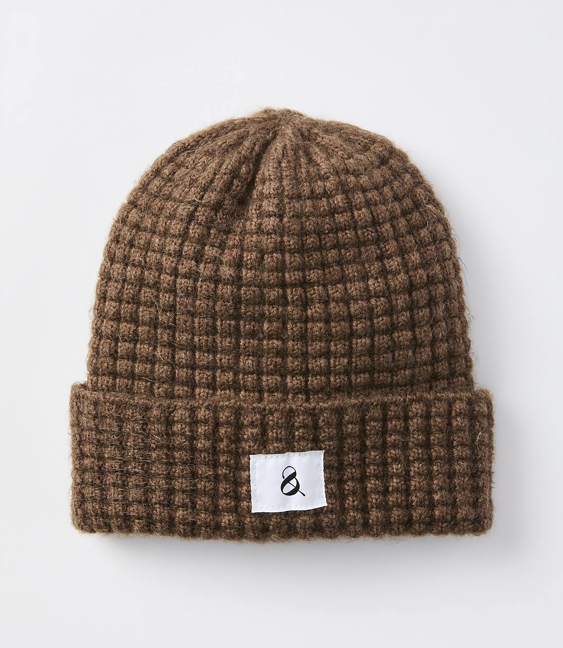 A brown waffle-knit beanie with a white tag featuring a black ampersand sits against a plain white background.