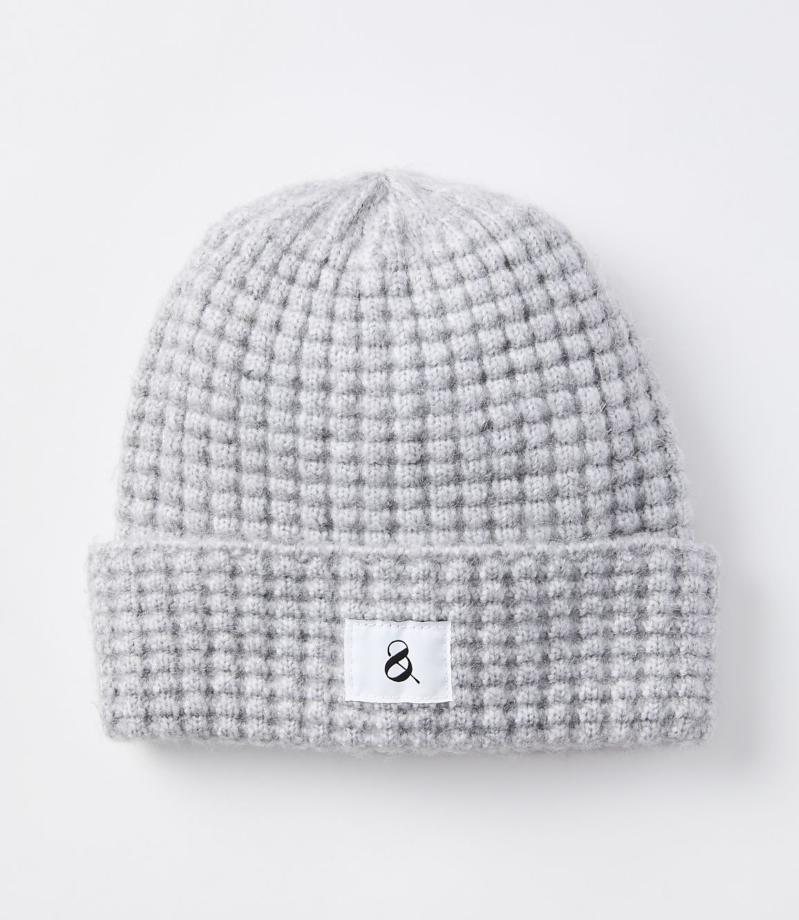 A light gray knitted beanie with a waffle knit pattern and a white tag with a black ampersand sits on a plain white background.