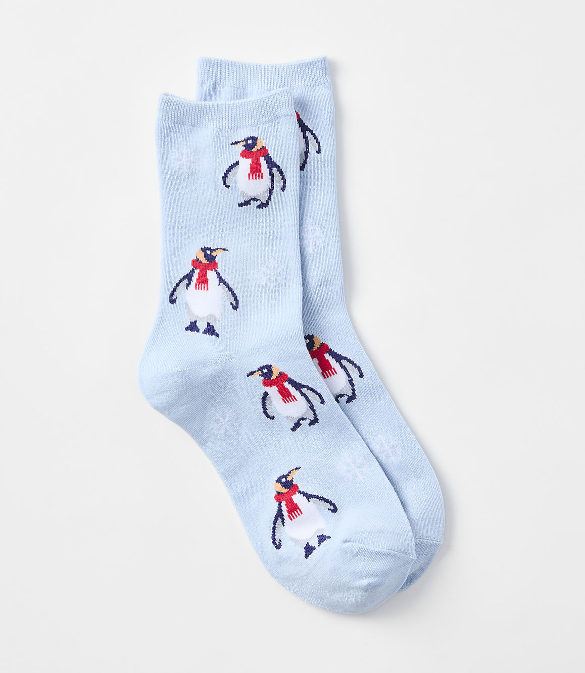 A pair of light blue socks with a pattern of penguins wearing red scarves and snowflakes are laid out against a plain white background.