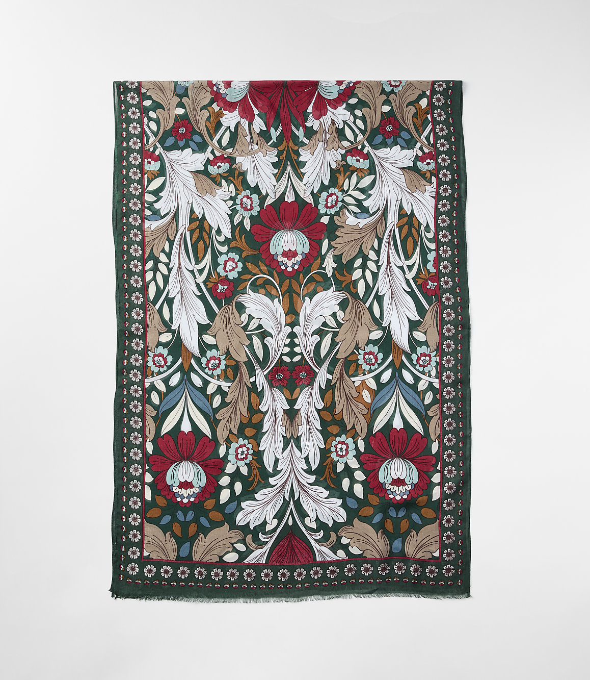 A richly patterned scarf with a dark green border and a central floral design of red, white, and brown elements is laid flat against a plain white background.