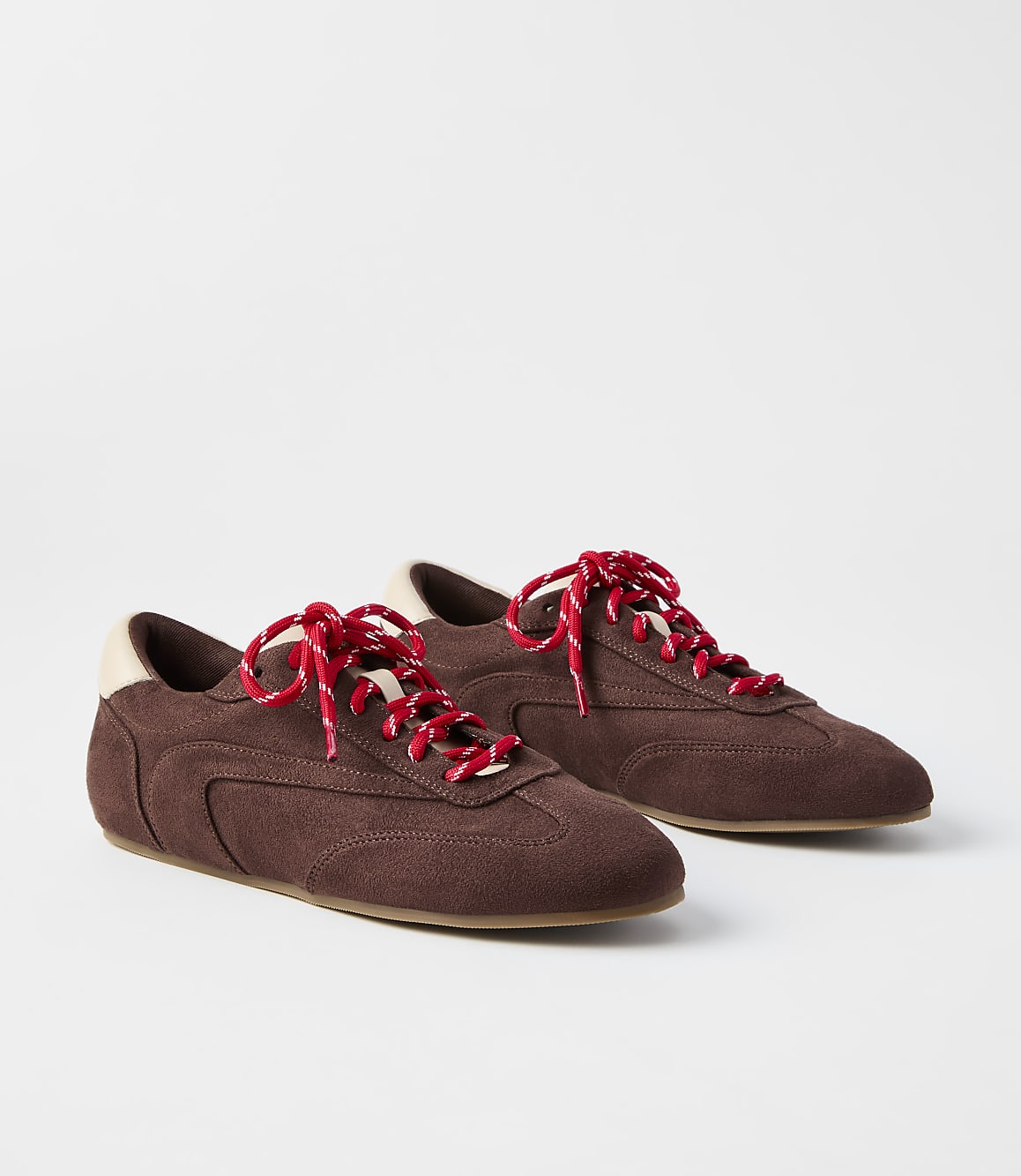 A pair of brown suede sneakers with red laces rests on a plain white background.
