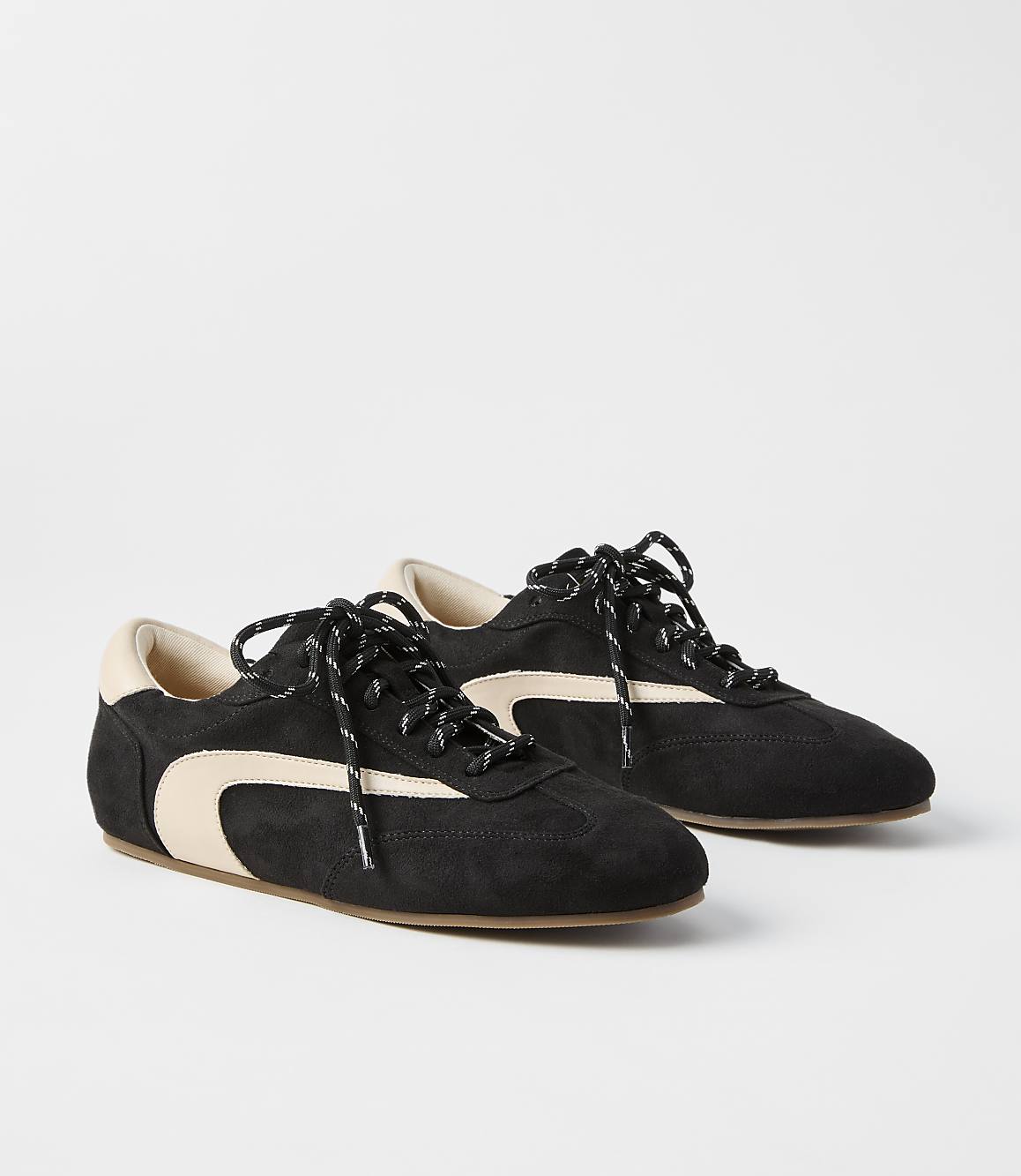 A pair of black suede sneakers with cream accents and black laces rests on a plain white background.