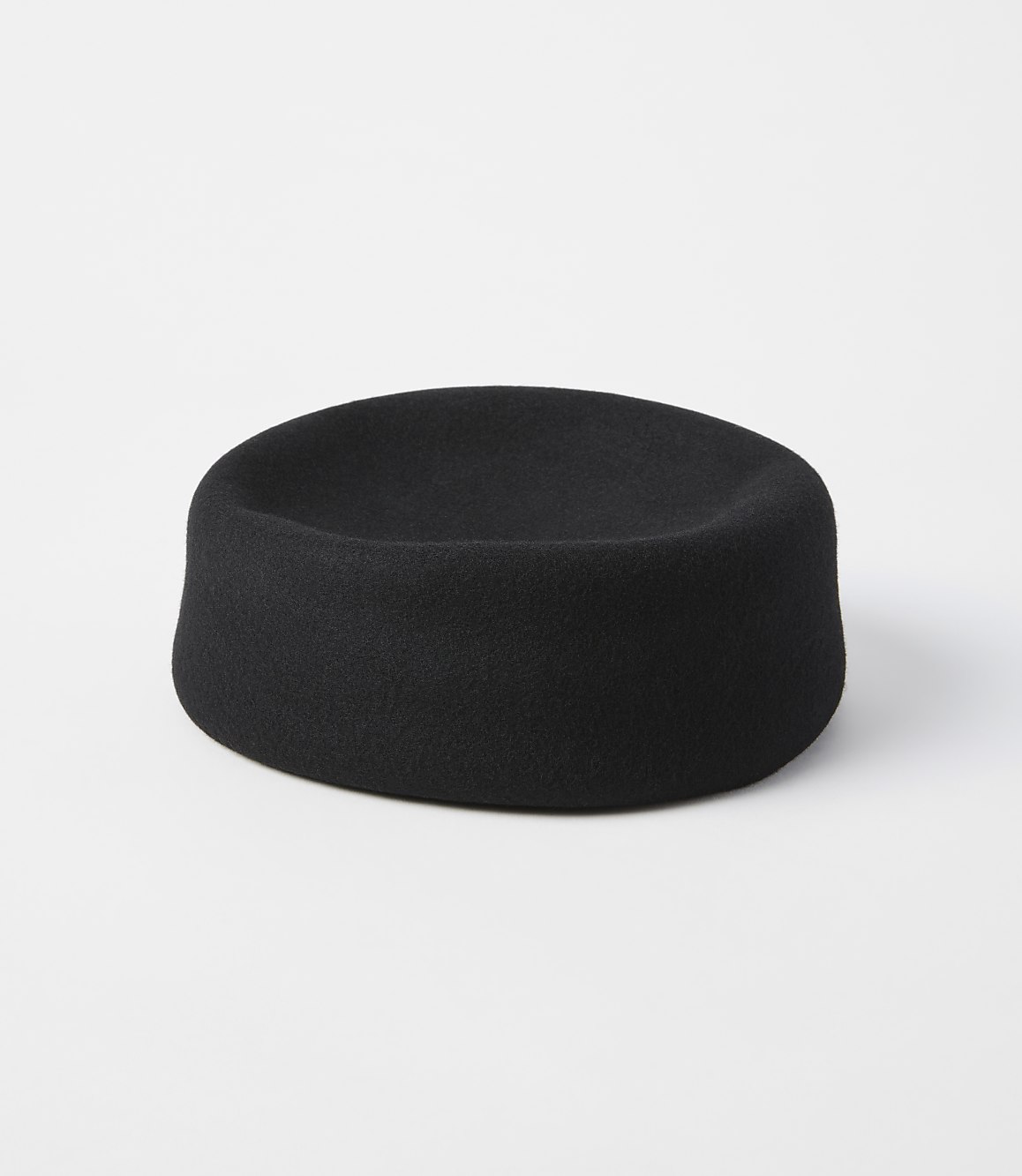 A black felt hat with a shallow crown sits on a white surface against a plain white background.