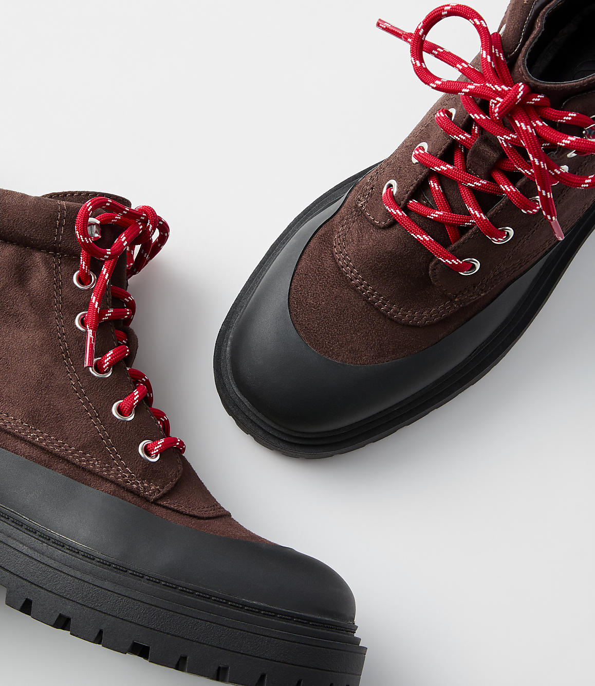 A pair of brown lace-up boots with thick black soles and red laces are displayed against a plain white background.