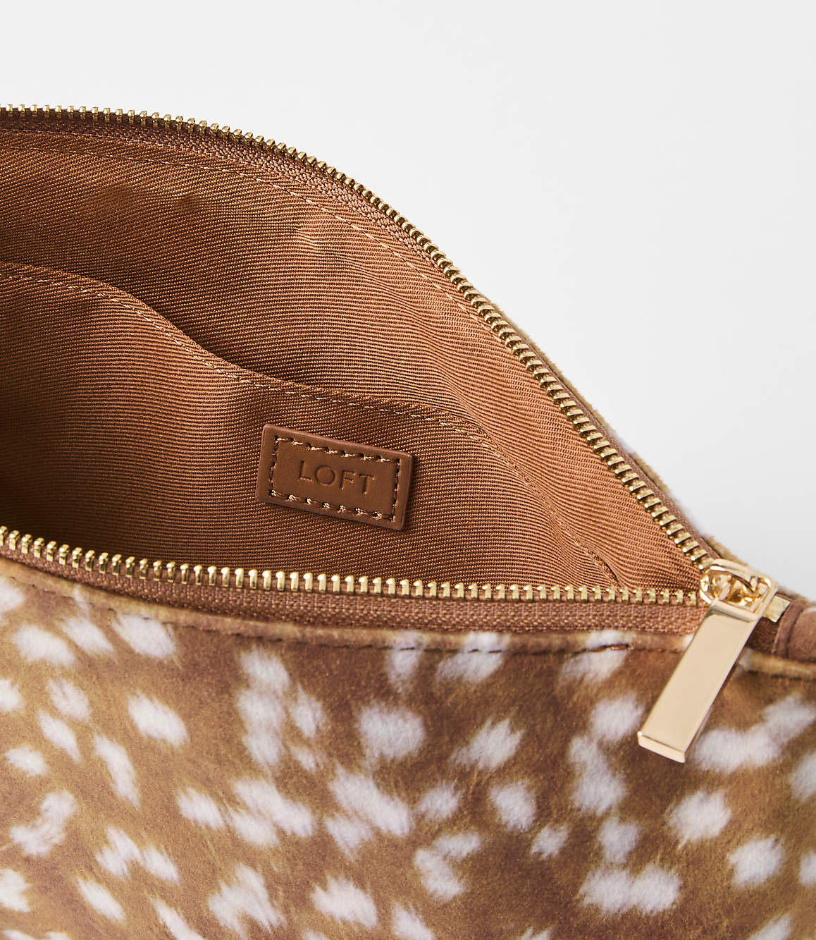 A fuzzy fawn-spotted clutch with a gold zipper is open against a plain white background.