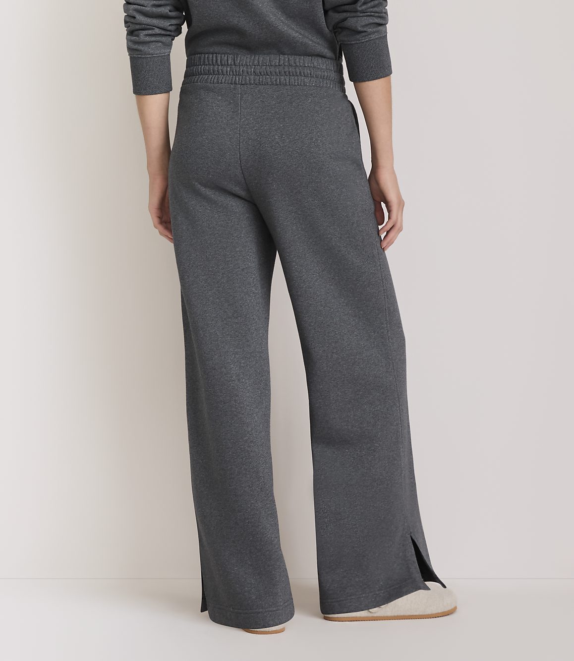 A person wearing dark gray sweatpants with split ankles stands on a light-colored floor against a plain, light background.