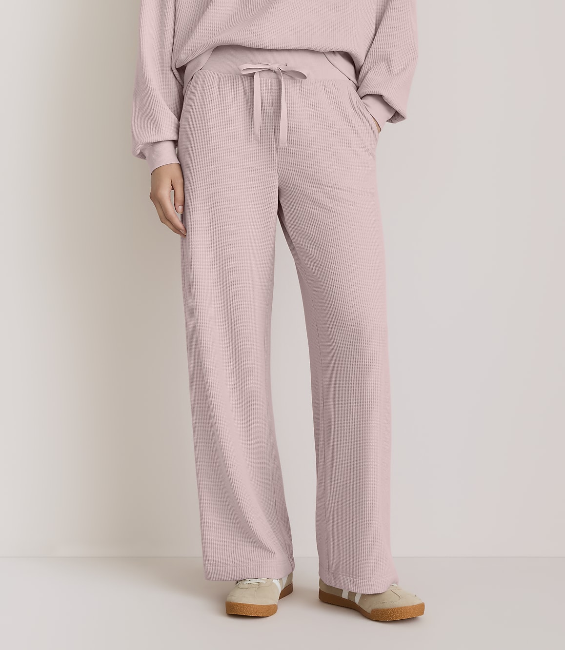 A person wearing pink ribbed lounge pants and sneakers stands against a plain, light-colored background.