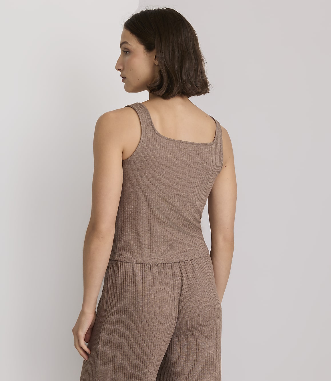 A woman in a brown ribbed tank top and matching pants stands against a plain, light-colored background.
