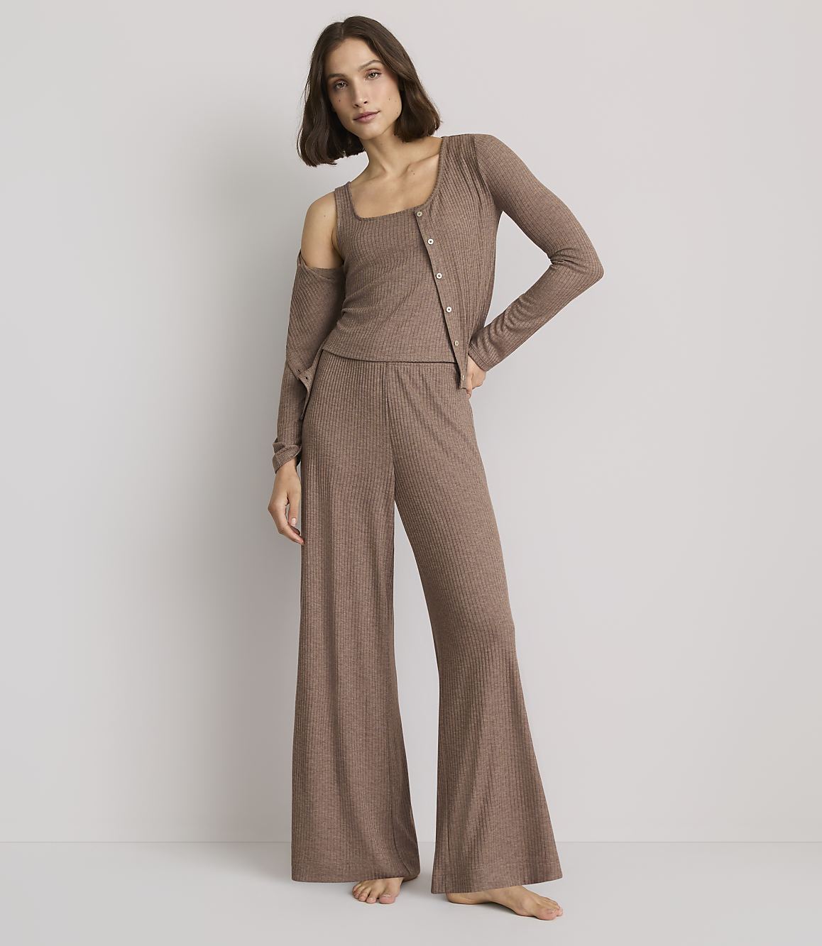 A woman in a brown ribbed loungewear set stands against a plain gray background.