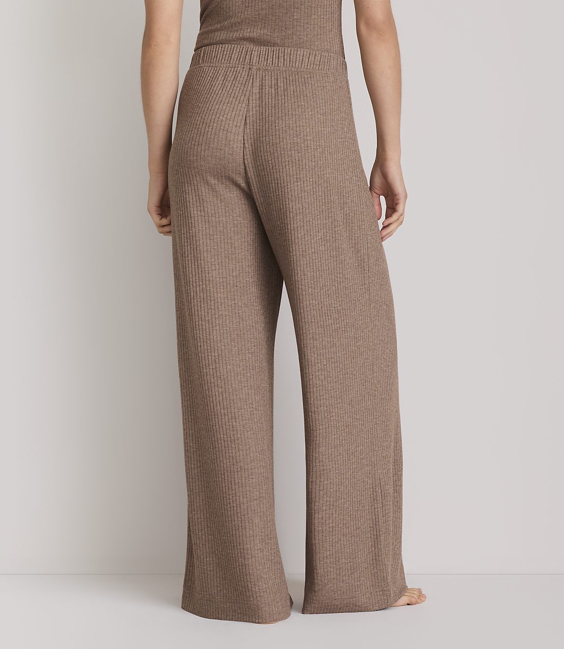 A person stands in ribbed brown wide-leg pants and a matching top against a plain white background.