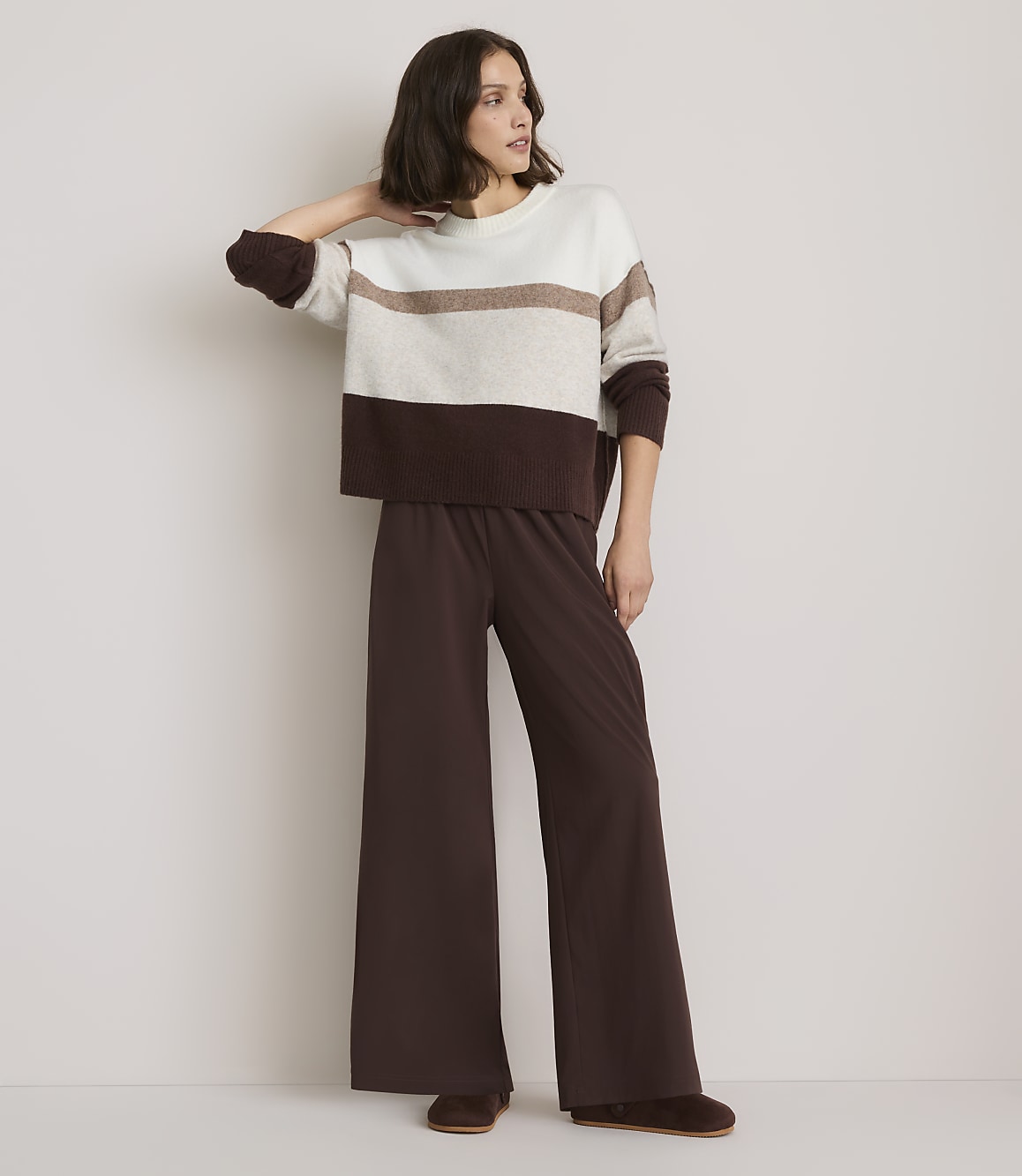 A woman in a striped sweater and wide-leg pants stands against a plain white background.