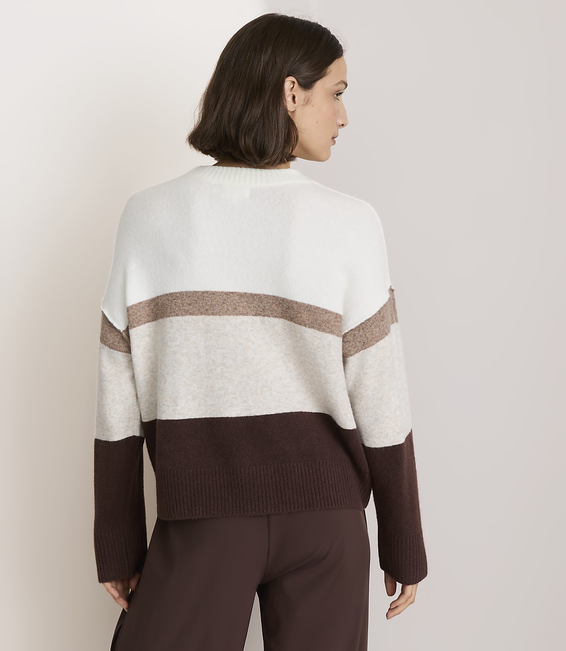 A woman in a striped sweater stands against a plain, light-colored background.