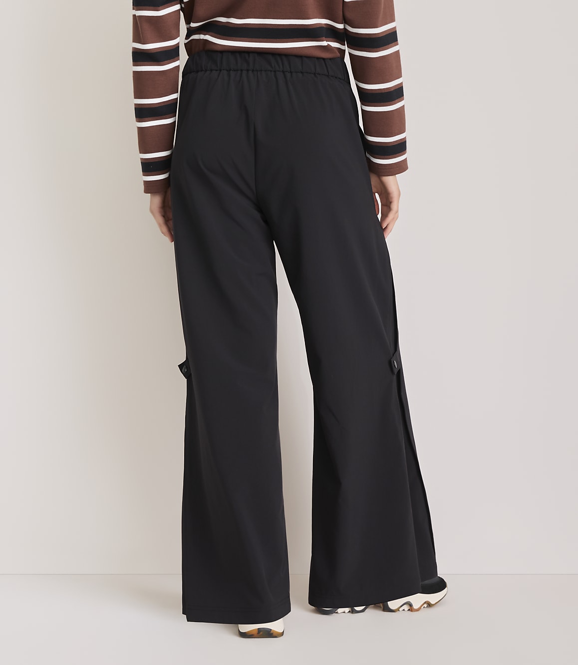 A person wearing black wide-leg pants with side slits and a striped long-sleeved shirt stands against a plain white background.